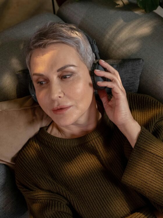 Music For Menopause: Woman in her 60s with short hair lying down with headphones on