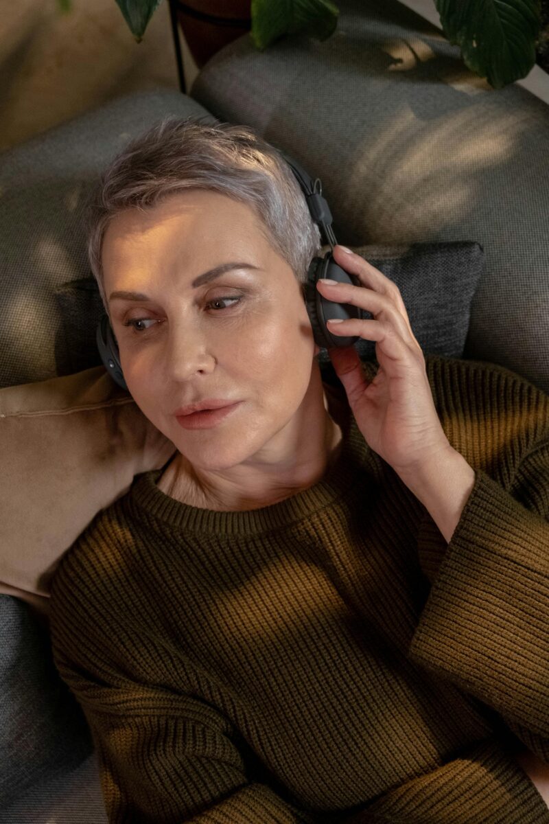 Music For Menopause: Woman in her 60s with short hair lying down with headphones on