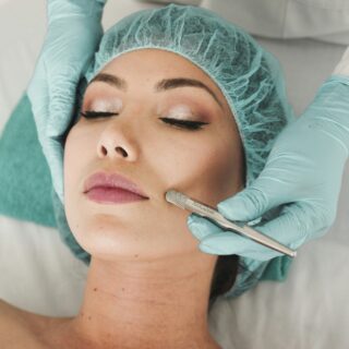 Facial Rejuvenation: Woman lying down with surgical cap on as someone is doing a procedure.