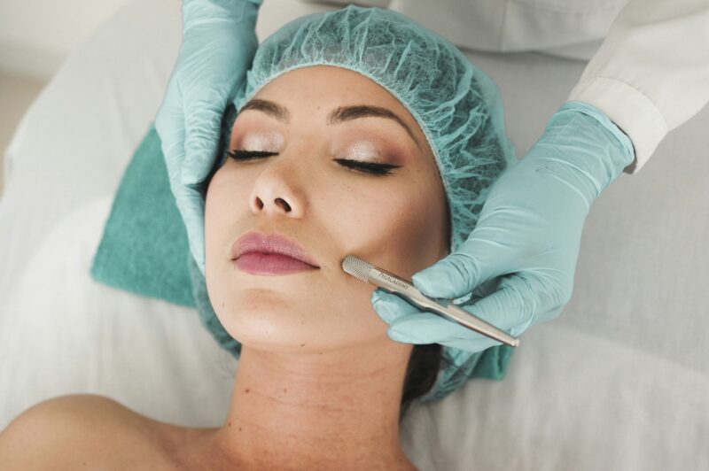 Facial Rejuvenation: Woman lying down with surgical cap on as someone is doing a procedure.