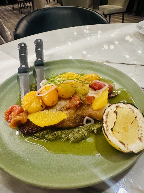 Vivo Avanti: Meluzzo - pan-seared cod, Pesto Siciliano, pickled shallot, stewed cherry tomato, lemon on a green plate with two knives