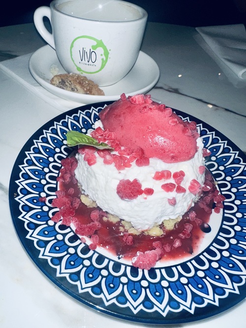 Vivo Avanti: Cheesecake Soffice - mousse, cornmeal crumble, berry & Balsamic compote and raspberry sorbet with small cup and saucer with biscotti in the background