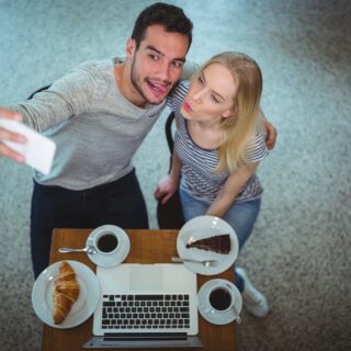 Digital Photos: Smiling young couple taking selfie while having coffee in a cafe