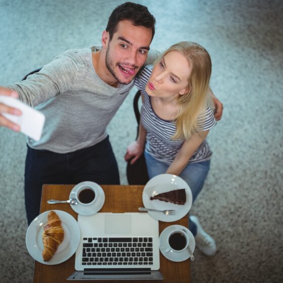Digital Photos: Smiling young couple taking selfie while having coffee in a cafe