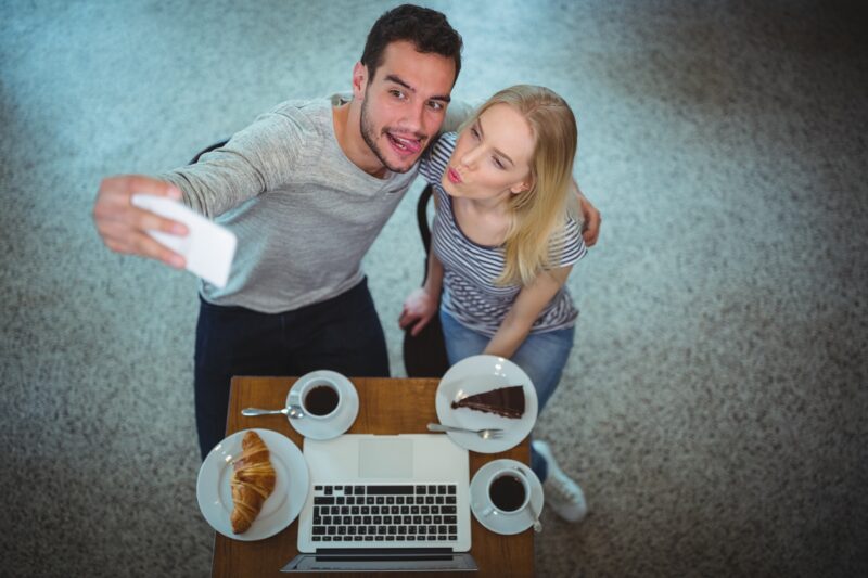 Digital Photos: Smiling young couple taking selfie while having coffee in a cafe