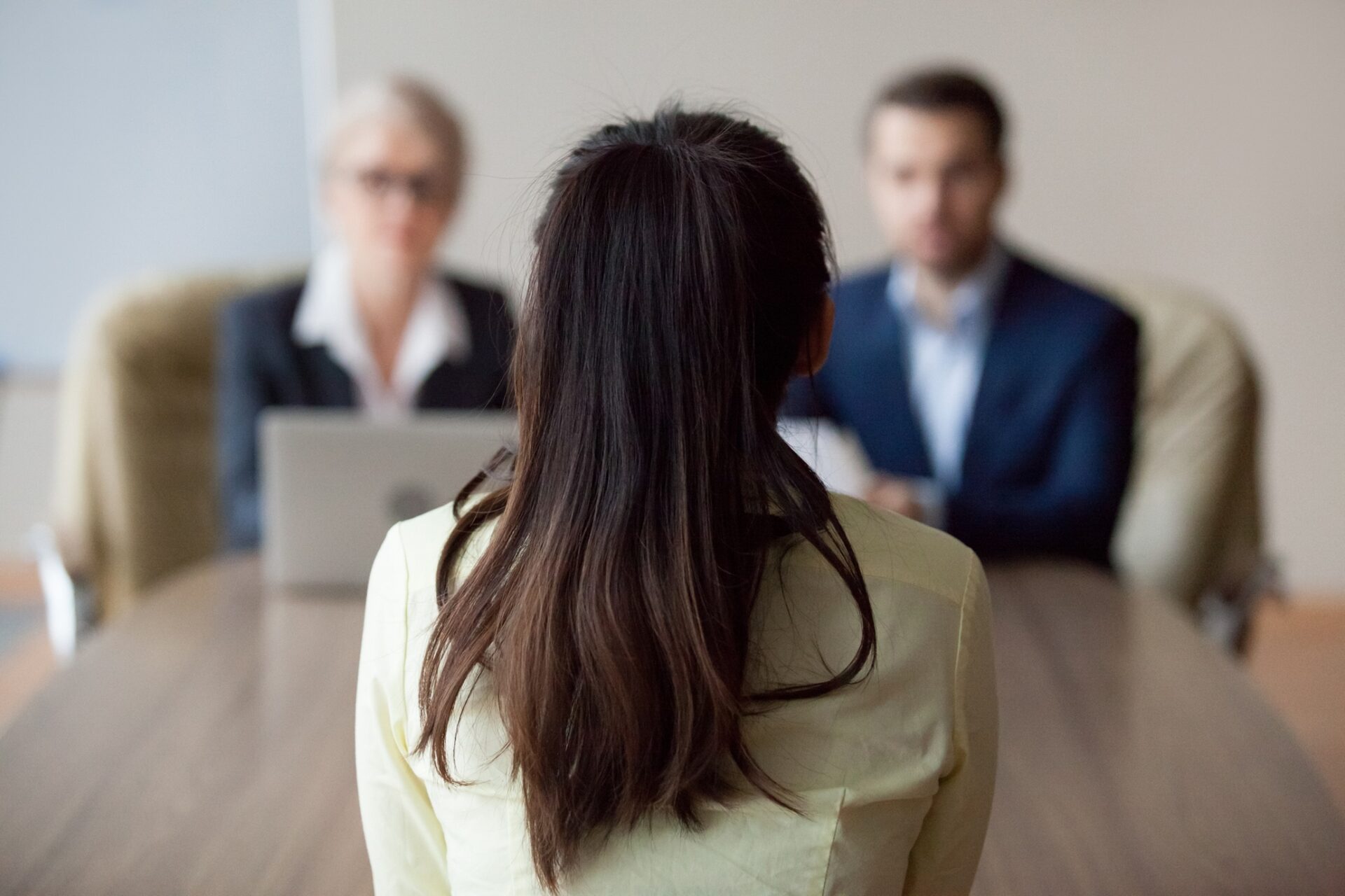 Employment: Businesswoman and businessman HR manager interviewing woman. Candidate female sitting her back to camera, focus on her, close up rear view, interviewers on background. Human resources, hiring concept