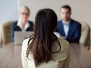 Employment: Businesswoman and businessman HR manager interviewing woman. Candidate female sitting her back to camera, focus on her, close up rear view, interviewers on background. Human resources, hiring concept