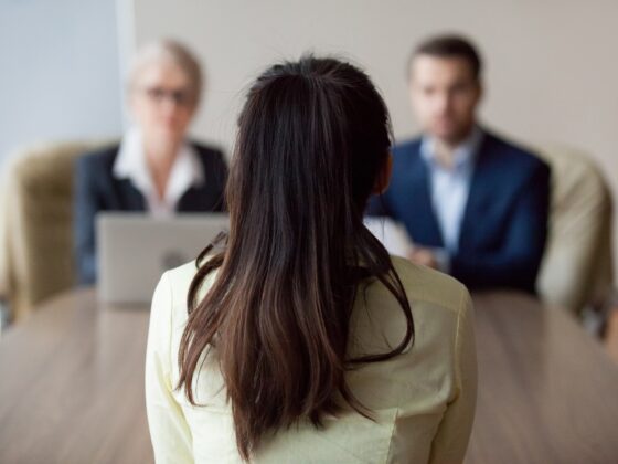 Employment: Businesswoman and businessman HR manager interviewing woman. Candidate female sitting her back to camera, focus on her, close up rear view, interviewers on background. Human resources, hiring concept