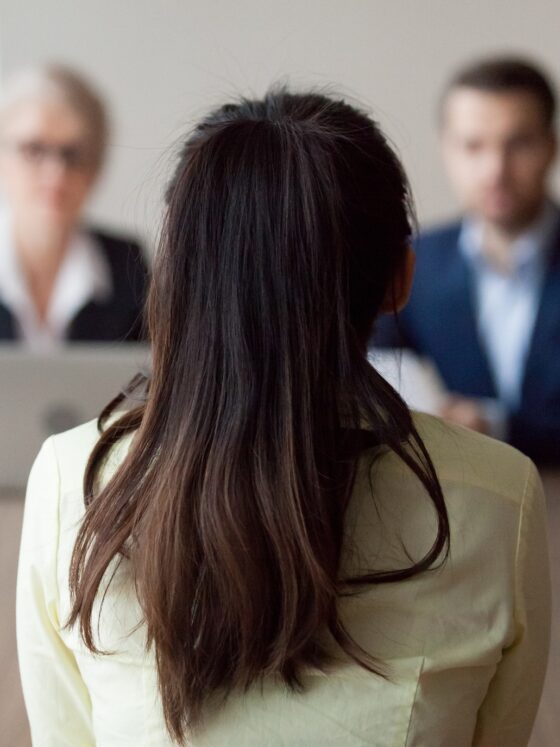 Employment: Businesswoman and businessman HR manager interviewing woman. Candidate female sitting her back to camera, focus on her, close up rear view, interviewers on background. Human resources, hiring concept