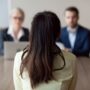 Employment: Businesswoman and businessman HR manager interviewing woman. Candidate female sitting her back to camera, focus on her, close up rear view, interviewers on background. Human resources, hiring concept