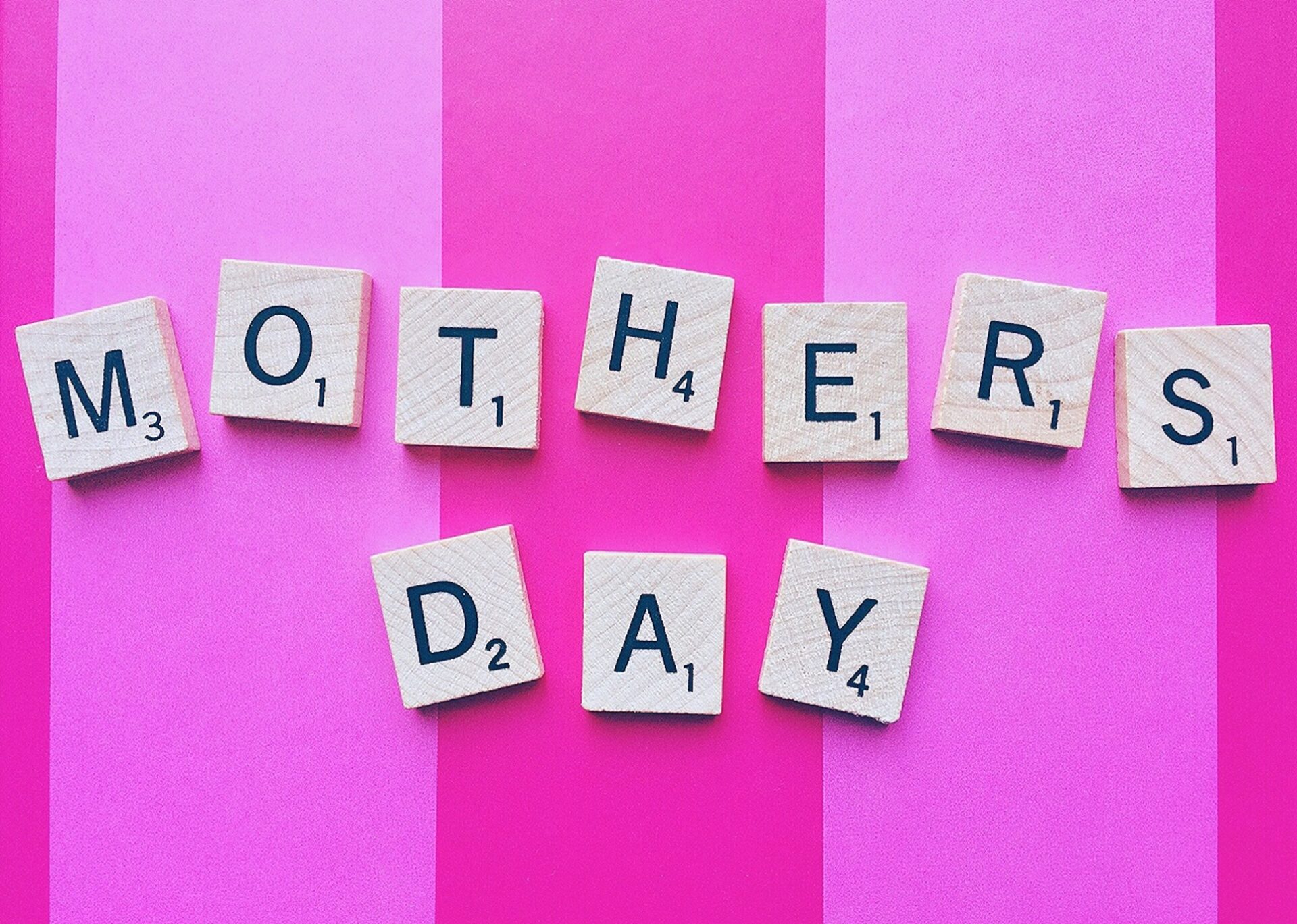 Gifts Your Mom Will Love: Mother's Day spelled out in Scrabble Tiles against a pink striped background