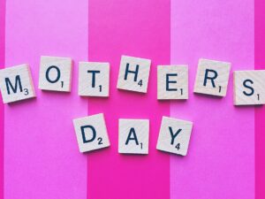 Gifts Your Mom Will Love: Mother's Day spelled out in Scrabble Tiles against a pink striped background