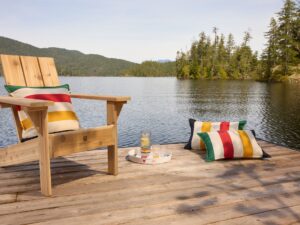 Hudson’s Bay Stripes Collection: Muskoka Chair with pillows and drinks on a tray near a lake