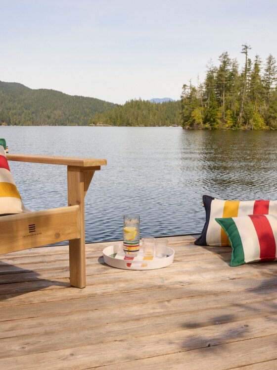 Hudson’s Bay Stripes Collection: Muskoka Chair with pillows and drinks on a tray near a lake