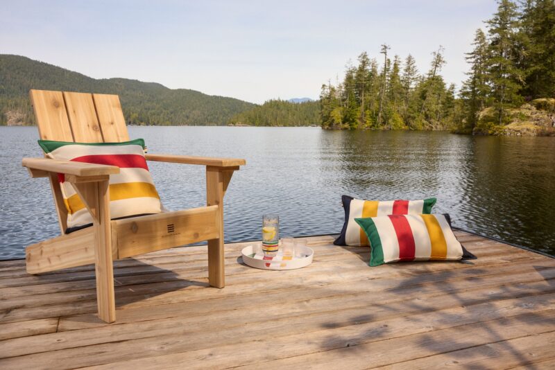 Hudson’s Bay Stripes Collection: Muskoka Chair with pillows and drinks on a tray near a lake