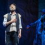 Fiddler On The Roof In Yiddish: Tevye singing with his hand over his heart with the fiddler in the background