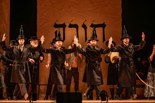 Fiddler on the Roof in Yiddish: Group of men dancing with wine bottles on their heads in front of a backdrop with Torah written in Hebrew