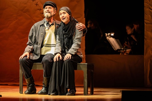 Fiddler On The Roof In Yiddish: Tevye and Golde sitting together on a bench.