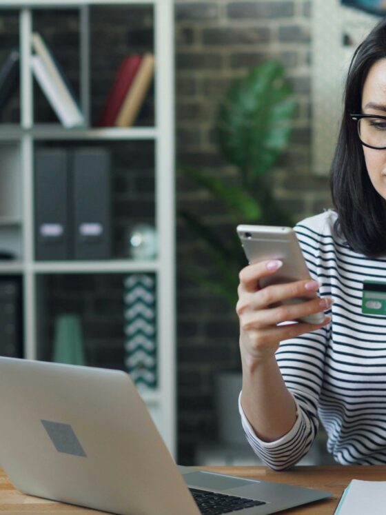 Pay Online: Woman in front of a laptop holding her mobile phone and bank card