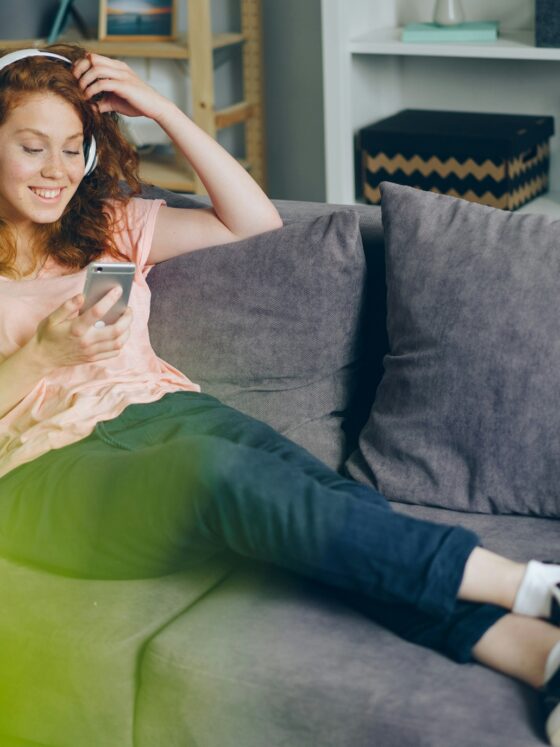 Entertainment Apps: woman on her couch with headphones and her cell phone
