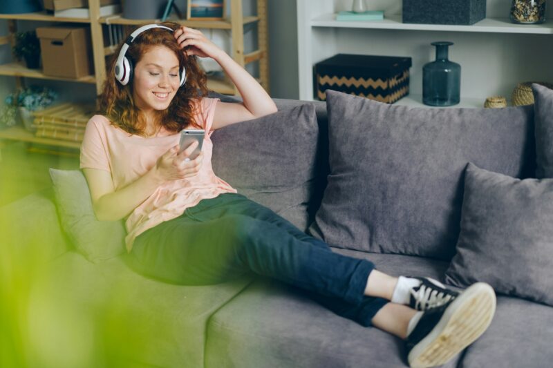 Entertainment Apps: woman on her couch with headphones and her cell phone
