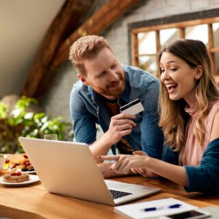 Credit Card: Happy woman pointing on something on laptop screen while shopping on the internet with her husband at home.