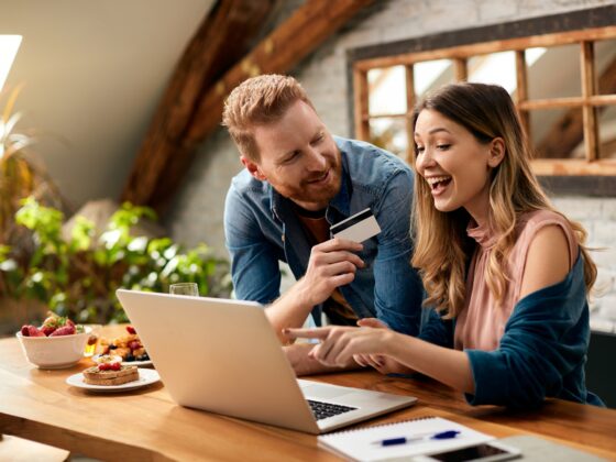 Credit Card: Happy woman pointing on something on laptop screen while shopping on the internet with her husband at home.