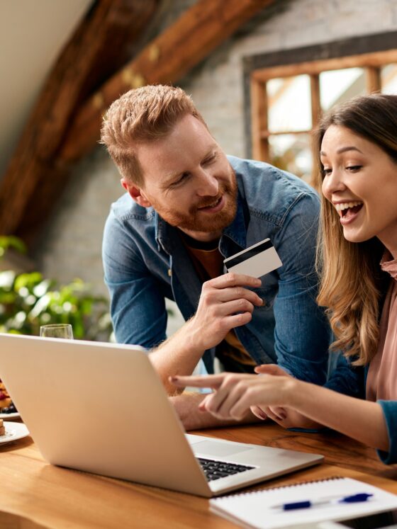 Credit Card: Happy woman pointing on something on laptop screen while shopping on the internet with her husband at home.