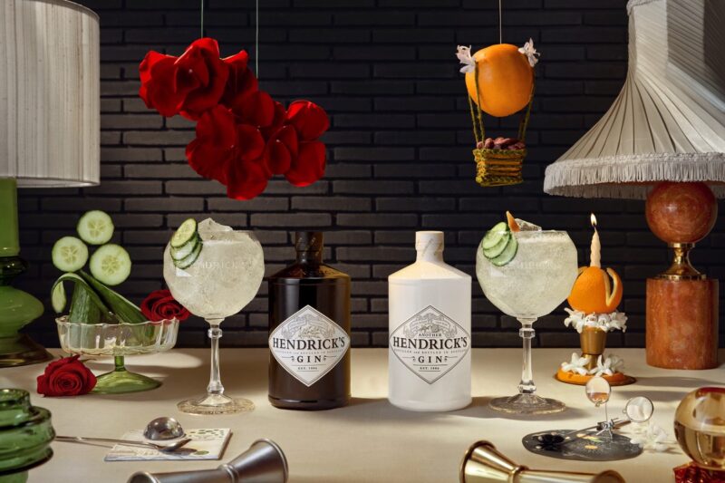 Hendrick's: Two bottles of Hendrick's Gin - one white and one black each with a cocktail beside it and cucumber, roses and an orange in the background