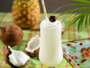 Piña Colada: Cocktail on picnic blanket with coconut and pineapple next to it