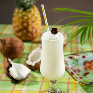 Piña Colada: Cocktail on picnic blanket with coconut and pineapple next to it
