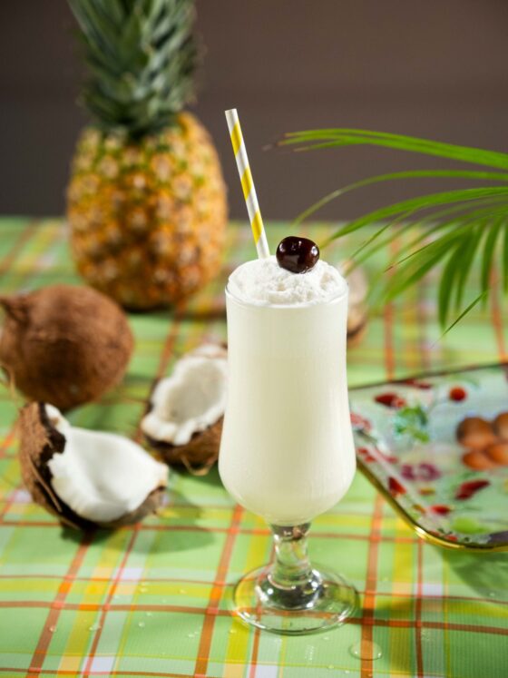 Piña Colada: Cocktail on picnic blanket with coconut and pineapple next to it