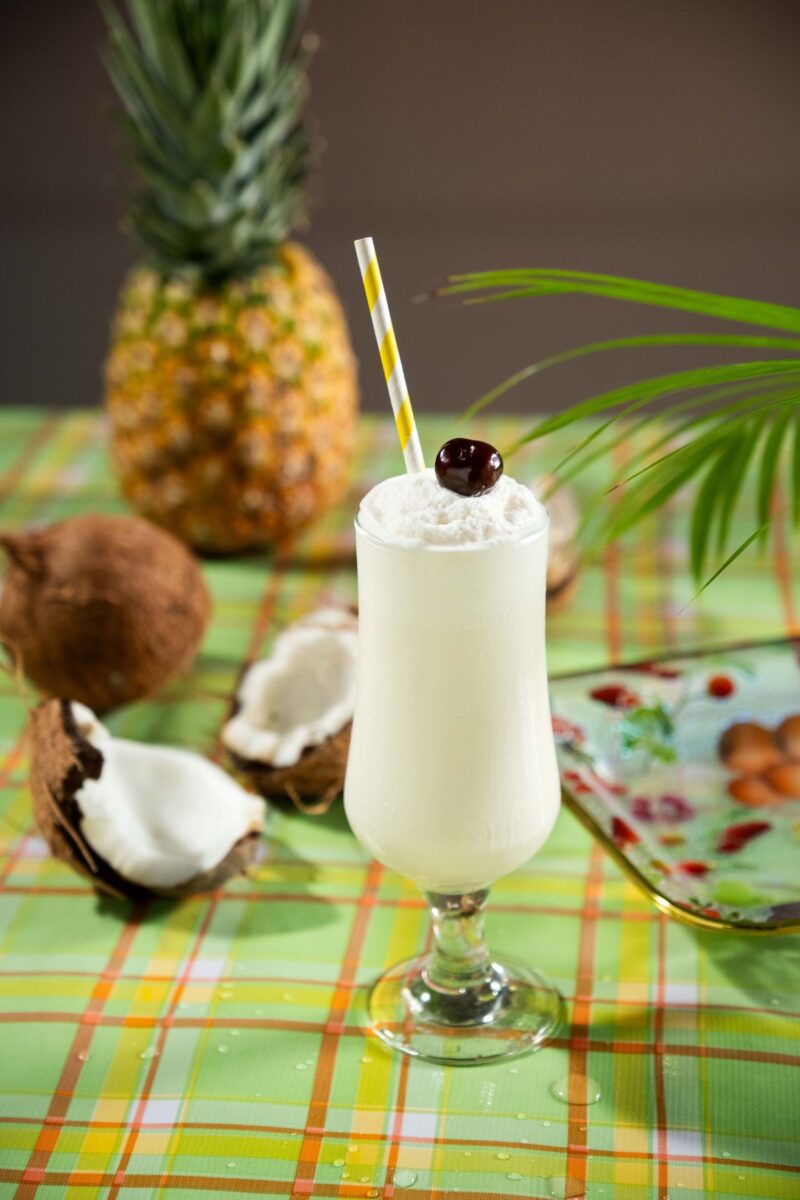 Piña Colada: Cocktail on picnic blanket with coconut and pineapple next to it