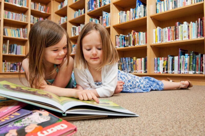 Best Kids' Books: two little girls in front of a pile of books at the library