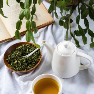 Green Tea Extract: Tea pot next to tea cup with green tea, loose leaves in a bowl next to a plant