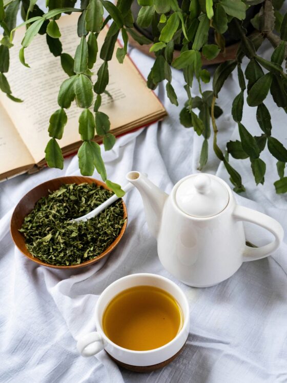 Green Tea Extract: Tea pot next to tea cup with green tea, loose leaves in a bowl next to a plant