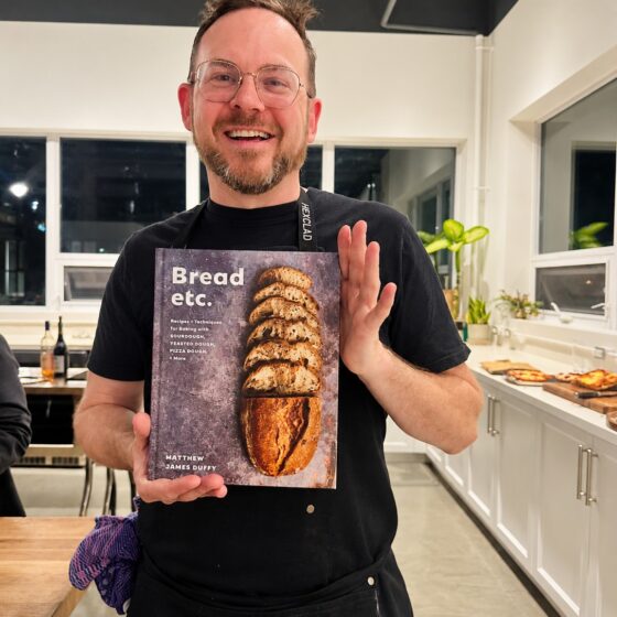 Sourdough: Matthew James Duffy in a commercial kitchen holding a copy of his cookbook, Bread, etc.