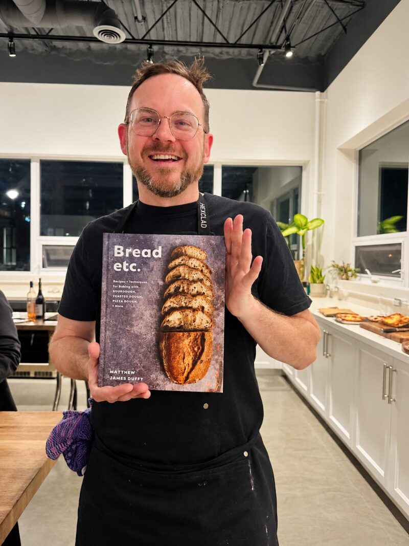 Sourdough: Matthew James Duffy in a commercial kitchen holding a copy of his cookbook, Bread, etc.