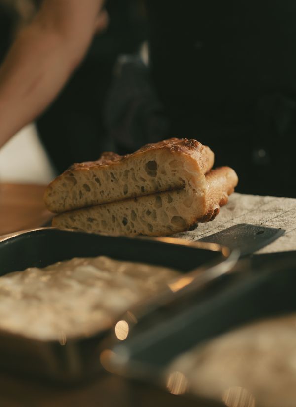Sourdough: close up of two pieces of cut focaccia with pan filled with dough in the forefront