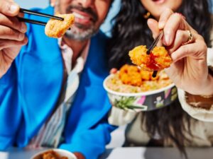 Calamari: Couple holding Thai Express Bowls with food on chopsticks