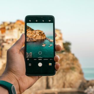 iPhone 18 Pro Max: Hand holding a smartphone to photograph a rocky coastline and the sea