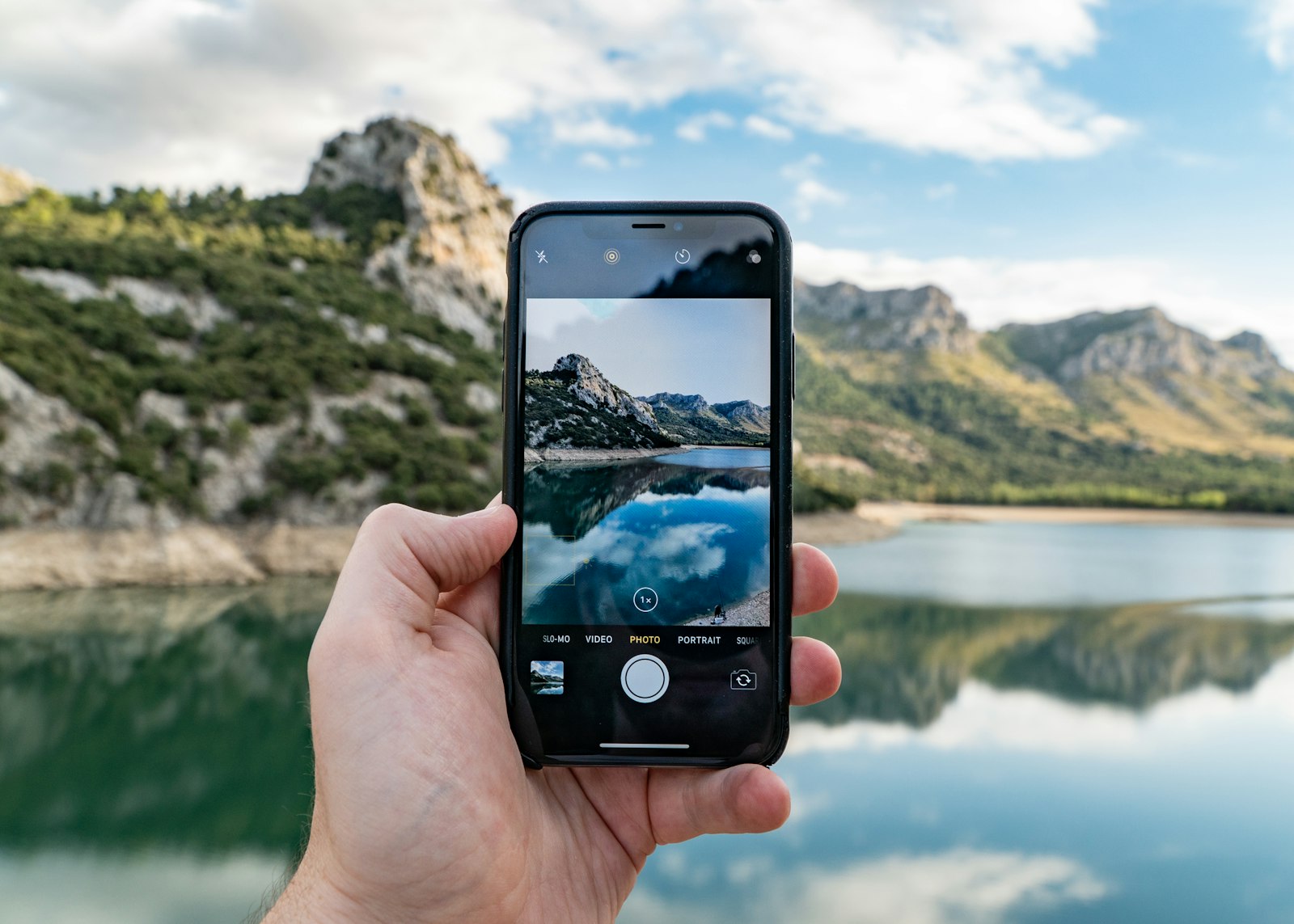 Téléphone tenu à la main pour photographier un lac et des montagnes